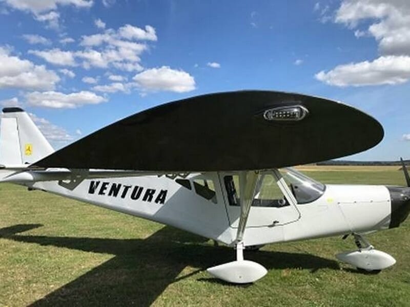 Avion ULM blanc avec ailes noires marqué Ventura, posé sur une piste d'herbe lors d'une initiation ULM près de Fontainebleau.