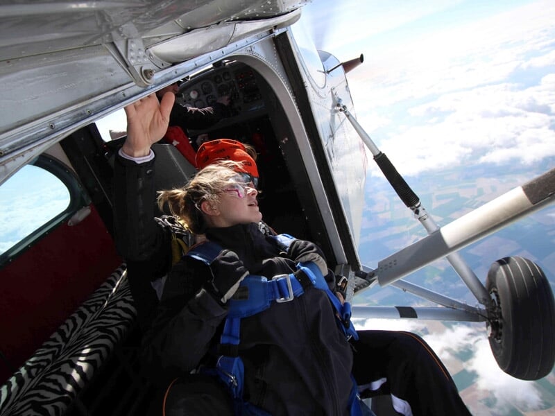 Une personne prête à sauter en parachute depuis un petit avion en vol, tenant la porte ouverte.