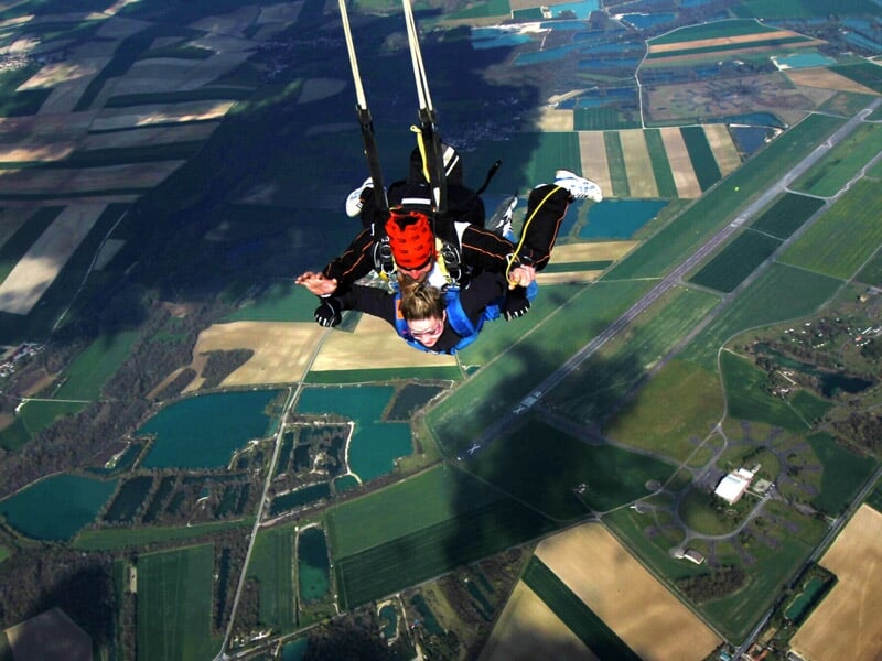 Saut en parachute en tandem au-dessus d'un aérodrome avec vue sur les champs et les pistes.