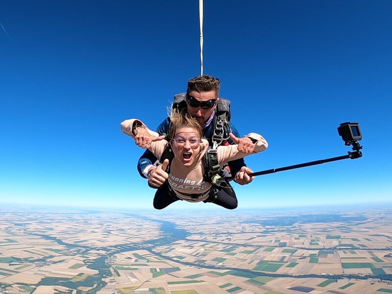 Deux personnes en chute libre en tandem avec une caméra fixée sur un bras pour filmer le saut.