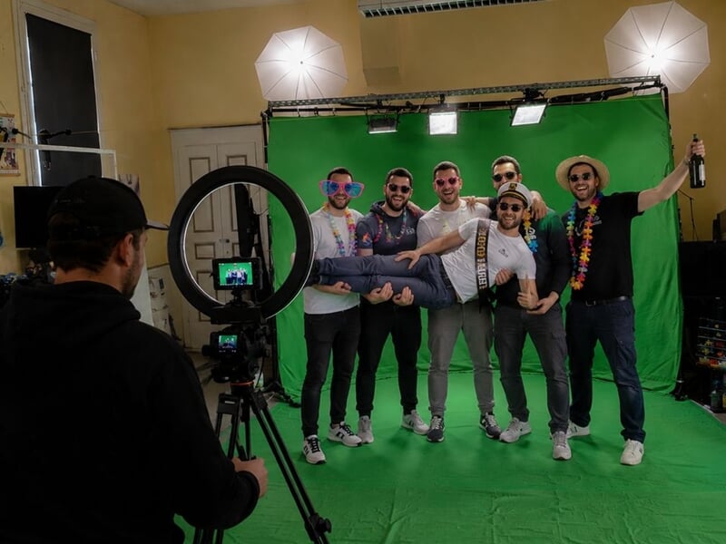 Un groupe d'amis pose joyeusement devant un fond vert dans un studio photo avec un photographe en action.