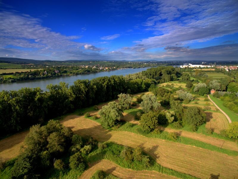 Vue aérienne d'un paysage rural avec champs, arbres et une rivière serpentant à travers la vallée sous un ciel partiellement nuageux