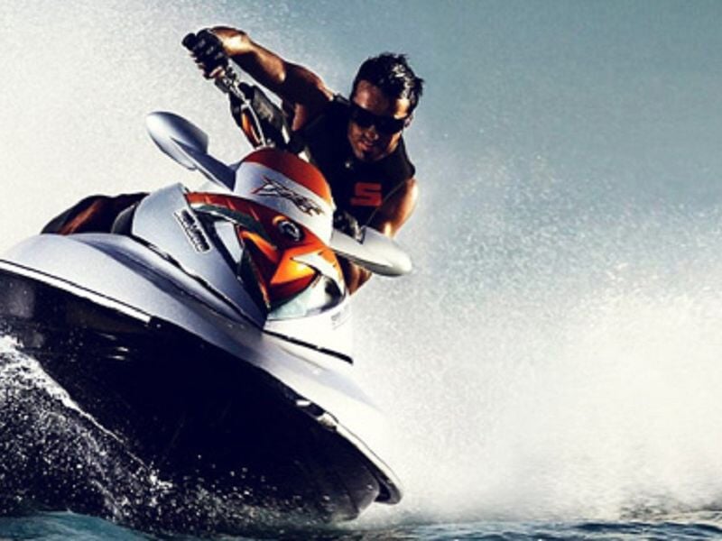 Homme en tenue sportive conduisant un jet ski blanc et orange sur une eau agitée avec éclaboussures.
