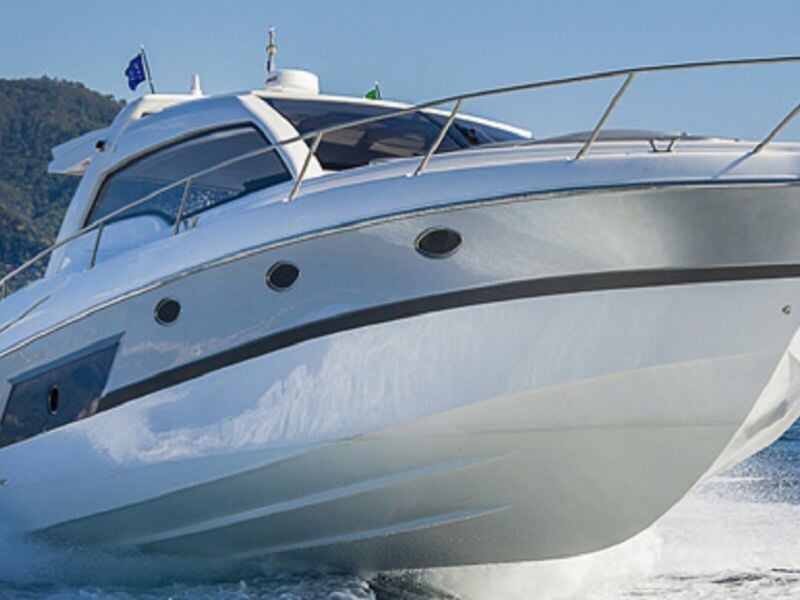 Grand yacht blanc naviguant sur une mer calme avec un ciel bleu et des collines en arrière-plan.