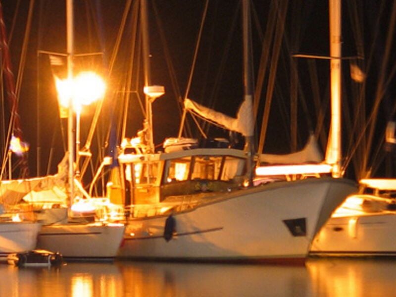 Bateaux amarrés dans un port la nuit avec des lumières jaunes illuminant les mâts et les ponts.