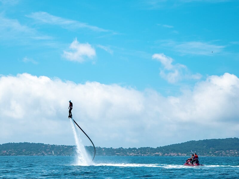 Flyboarder en hauteur au-dessus de la mer, propulsé par un jet d'eau, avec un bateau à moteur à proximité.