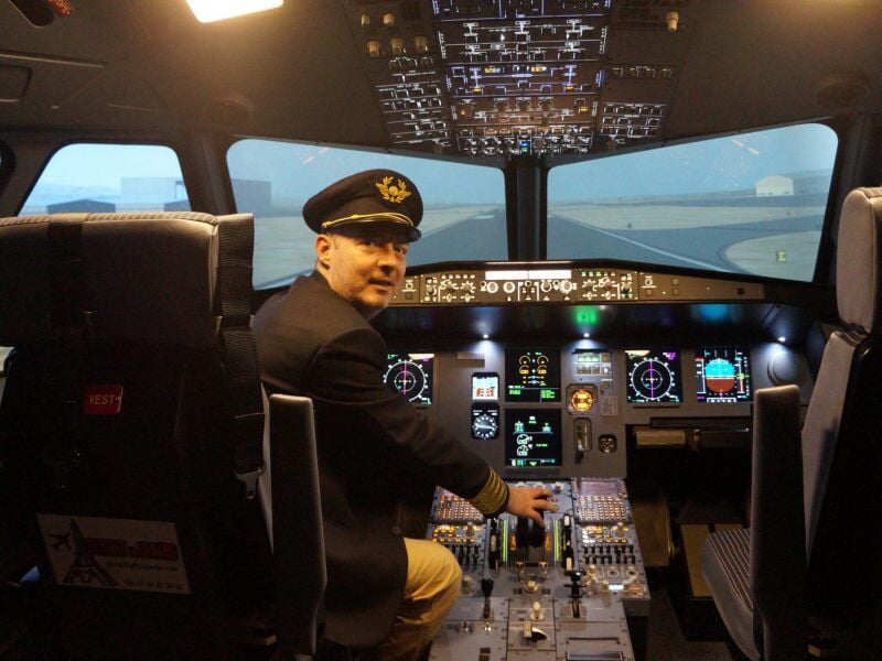 Homme en uniforme de pilote dans un simulateur de vol d'avion moderne avec tableau de bord éclairé.
