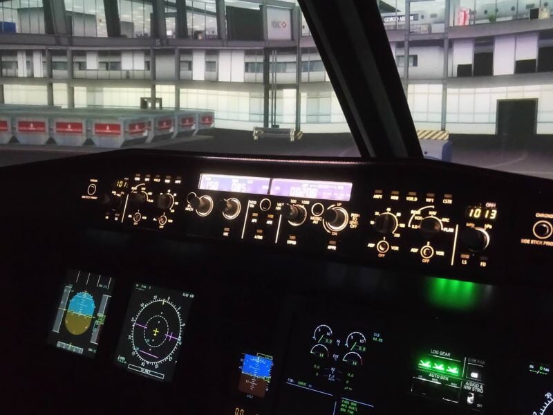 Cockpit de simulateur de pilotage d'avion avec écrans et commandes visibles dans un hangar