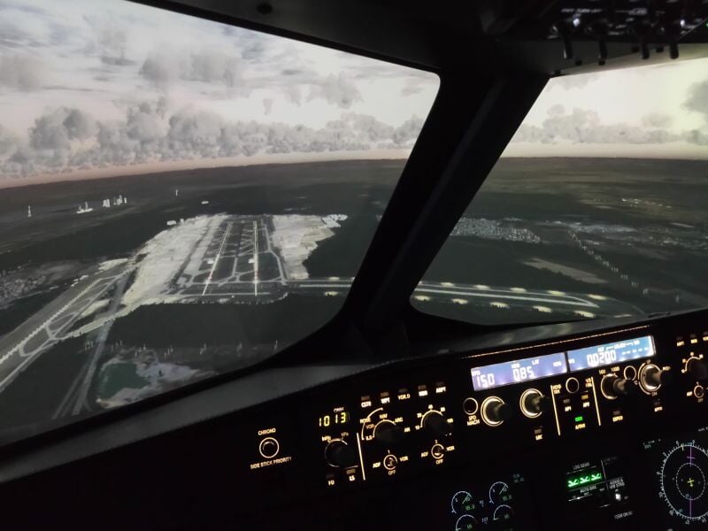 Vue depuis le poste de pilotage d'un simulateur d'avion survolant un aéroport au crépuscule.