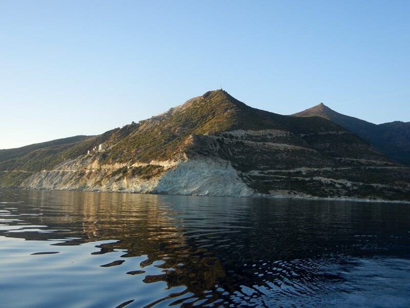 Montagne rocheuse se reflétant dans une eau calme au coucher du soleil, ambiance paisible et naturelle.