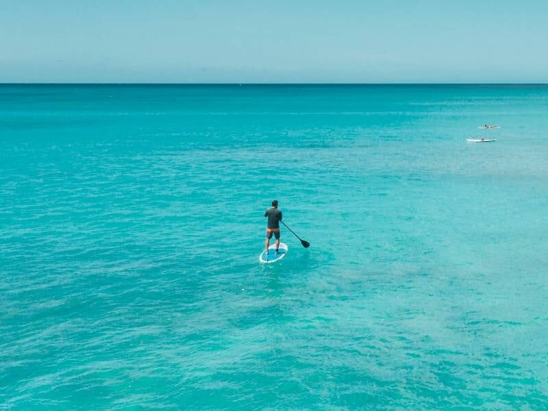 Homme pagayant sur un stand-up paddle sur une mer calme et turquoise, horizon dégagé et ciel clair.