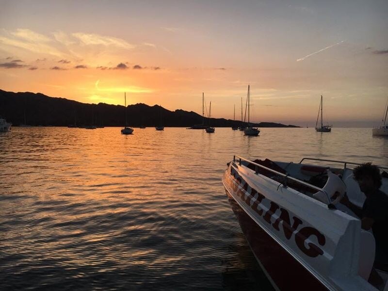 Bateaux à voile ancrés sur une mer calme au coucher du soleil avec des collines sombres en arrière-plan.