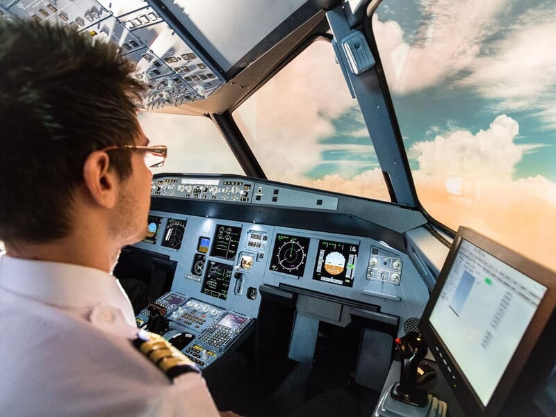 Homme pilote concentré dans un simulateur de vol d'avion avec vue sur ciel et instruments de bord modernes.