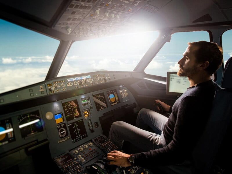 Homme assis dans un cockpit de simulateur d'avion, observant les instruments et le ciel à travers le pare-brise.