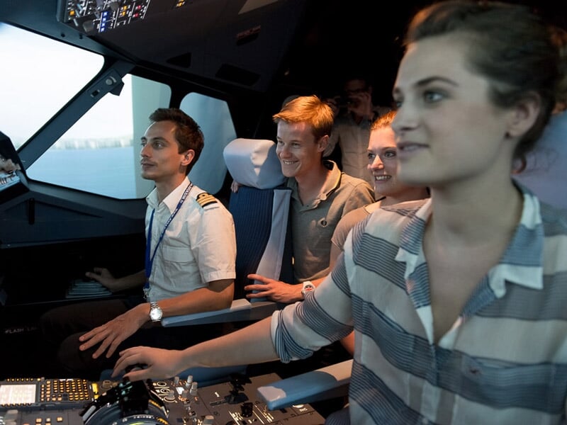 Groupe de jeunes dans un simulateur de vol, une femme aux commandes et plusieurs personnes souriantes à l'arrière.