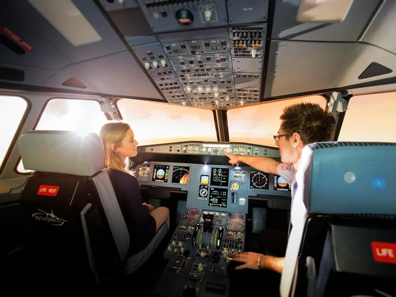 Deux personnes dans un simulateur d'avion, une femme et un homme discutent en regardant les instruments de bord.
