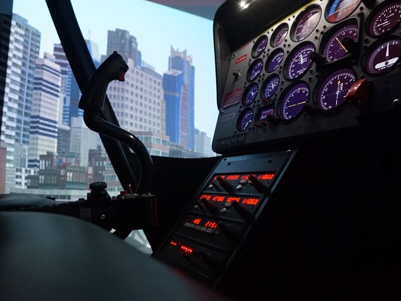 Cockpit d'un simulateur de vol avec instruments lumineux et vue sur une ville moderne en arrière-plan.