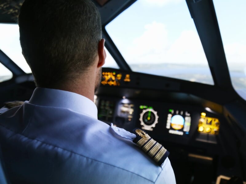 Vue arrière d'un pilote masculin en uniforme observant les instruments de vol dans un simulateur de cockpit d'avion