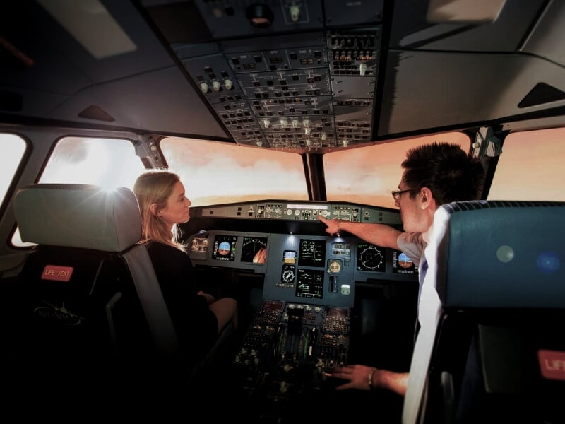 Deux personnes, un homme et une femme, dans un simulateur de cockpit d'avion de ligne, avec un échange sur les opérations de vol
