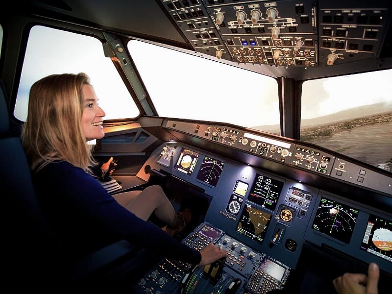 Pilote féminin souriant aux commandes dans un simulateur de cockpit d'avion de ligne avec des écrans multifonctions allumés