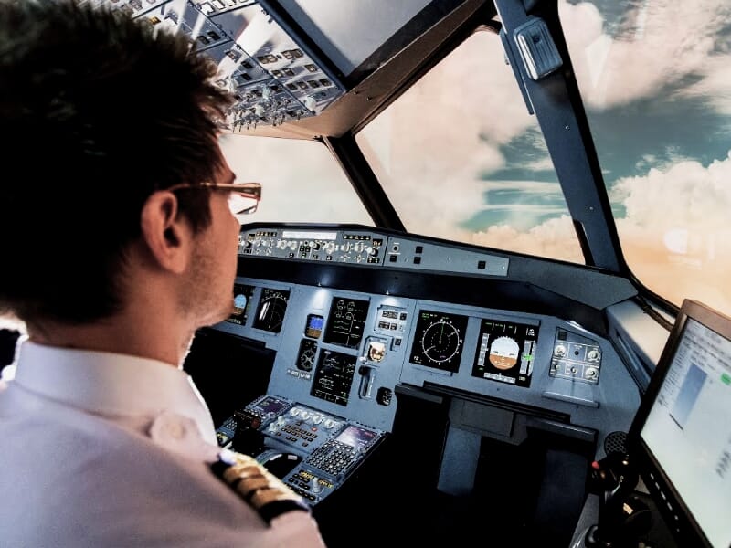 Pilote masculin en uniforme dans un simulateur de cockpit d'avion de ligne, avec vue sur les instruments de vol et les nuages à l'extérieur