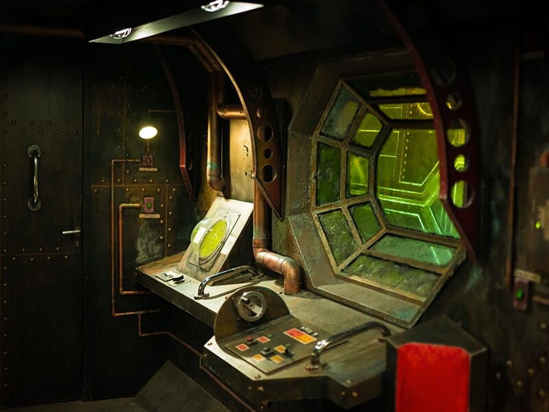 Poste de pilotage rétro-futuriste avec une fenêtre polygonale donnant sur un décor verdâtre.