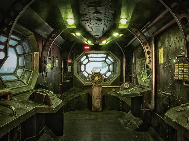 Intérieur d'une cabine métallique futuriste avec un volant central et des hublots polygonaux.