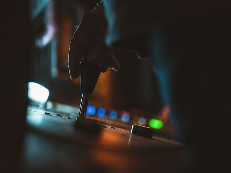Gros plan d'une main manipulant une manette de commande dans un environnement sombre éclairé par des boutons lumineux.