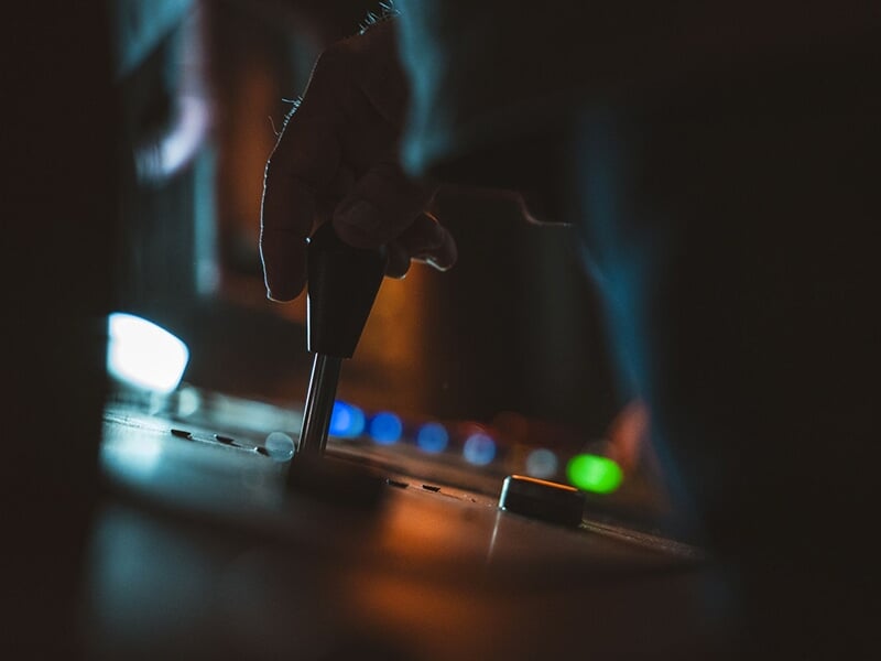 Gros plan d'une main manipulant une manette de commande dans un environnement sombre éclairé par des boutons lumineux.