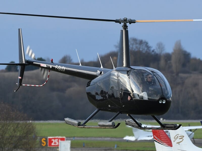 Hélicoptère noir en vol stationnaire près d'une piste avec un paysage flou en arrière-plan