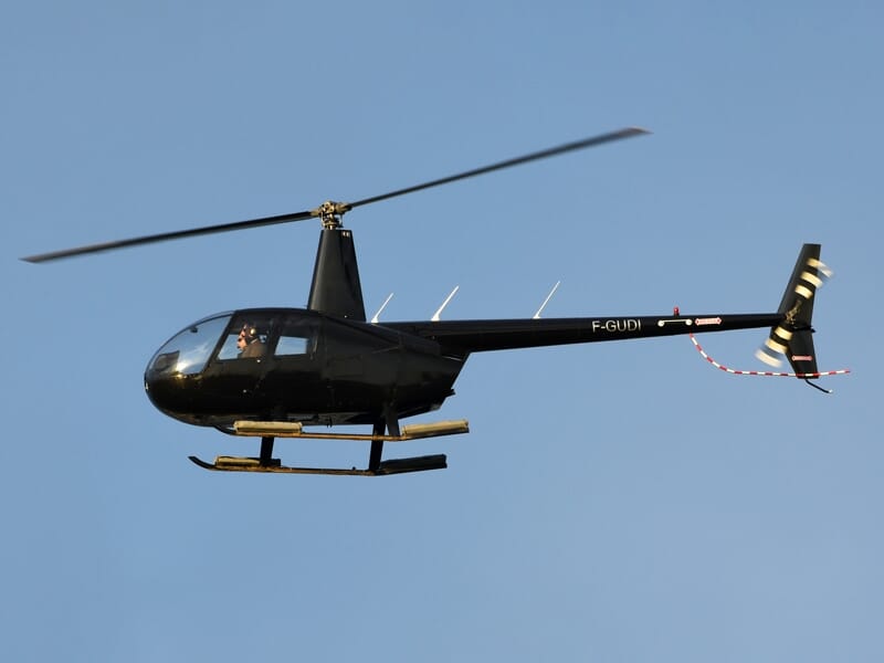 Hélicoptère noir en vol avec un ciel bleu clair et un pilote visible à bord