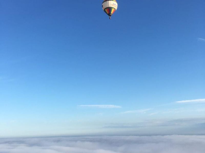 Montgolfière aux couleurs vives volant haut dans le ciel au-dessus d'une mer de nuages, avec un vaste ciel bleu s'étendant à l'horizon