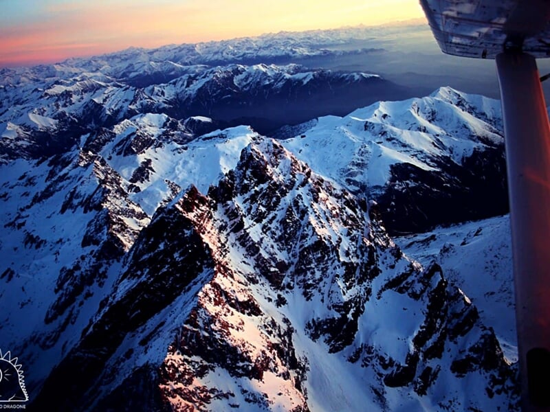 Vue aérienne de montagnes enneigées au coucher du soleil prise depuis un avion en vol au-dessus des Alpes.
