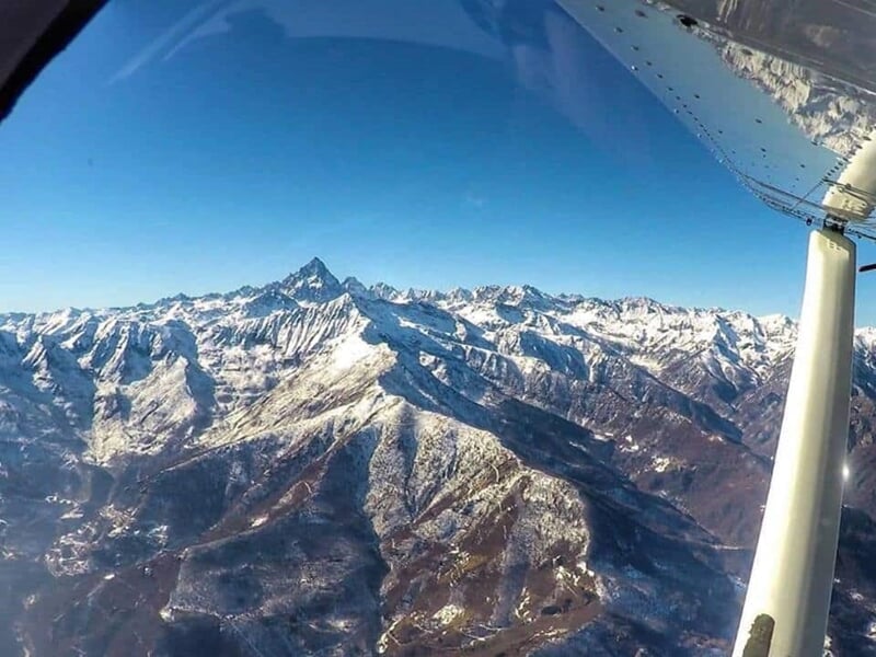 Paysage montagneux avec sommets enneigés vu depuis l'intérieur d'un petit avion léger en plein vol.