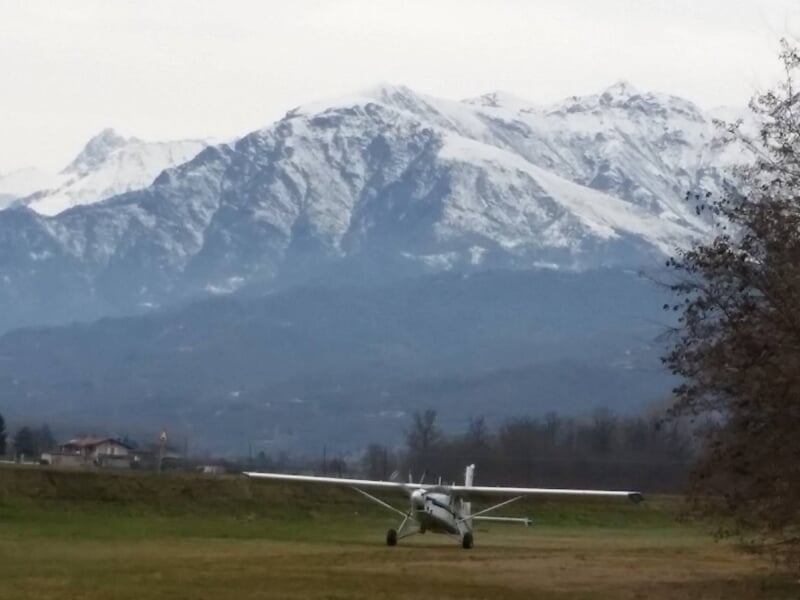 Petit avion posé sur une piste d'herbe avec une grande montagne enneigée en arrière-plan par temps clair.