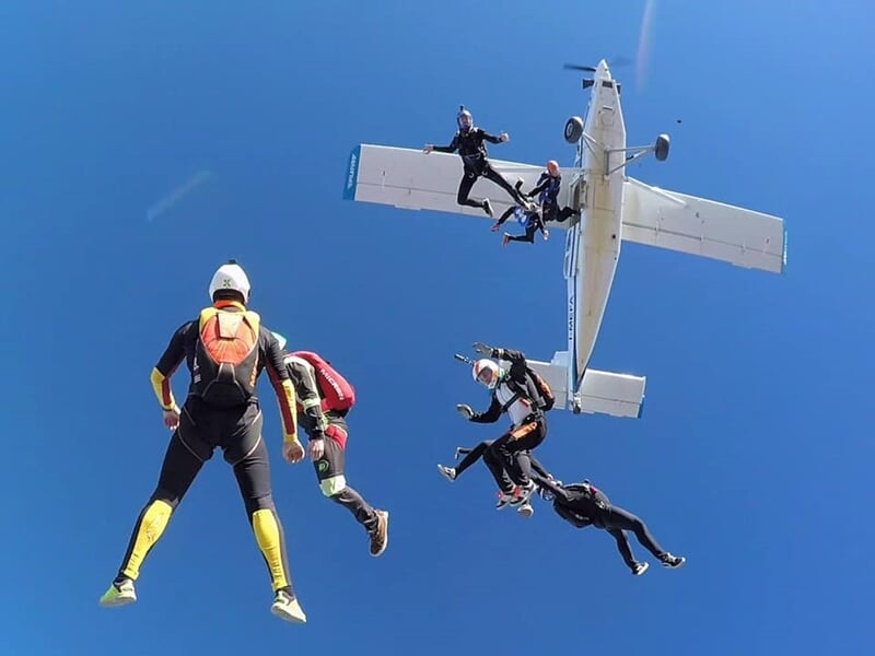 Groupe de parachutistes en chute libre sortant d'un avion blanc en plein ciel bleu lors d'un saut en tandem.