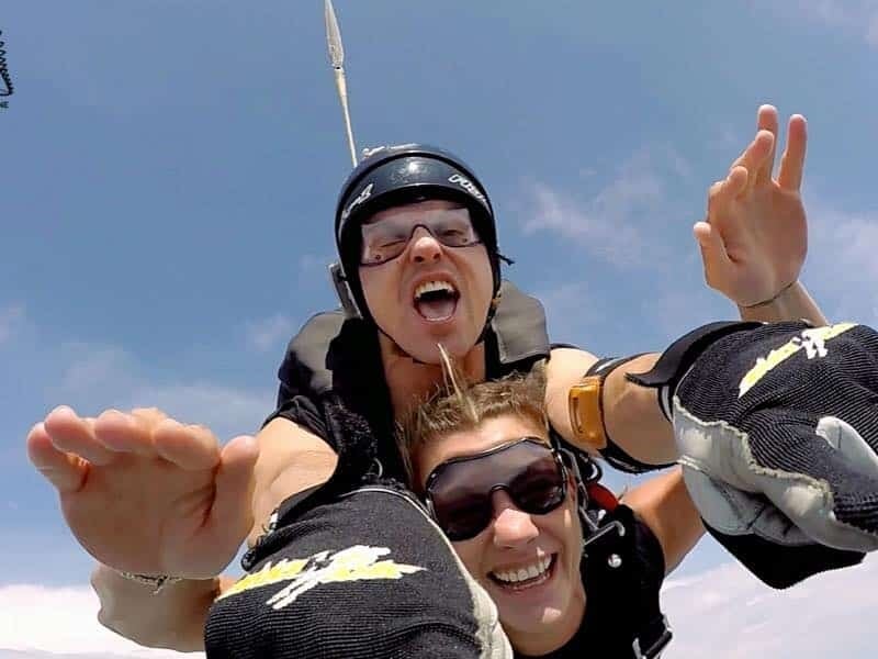 Saut en parachute tandem avec deux personnes souriantes en chute libre sous un ciel dégagé et ensoleillé.