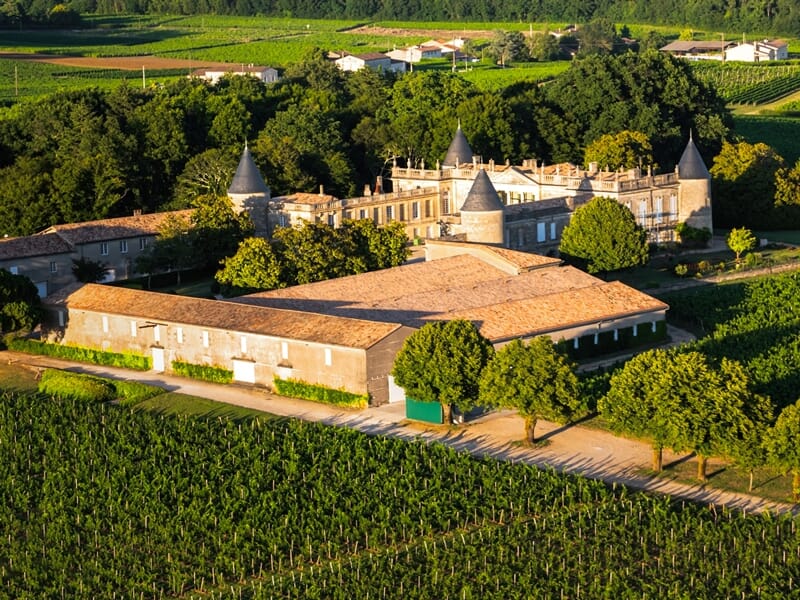 Vue aérienne d'un grand domaine viticole libournais avec des toits pointus et des vignobles environnants.