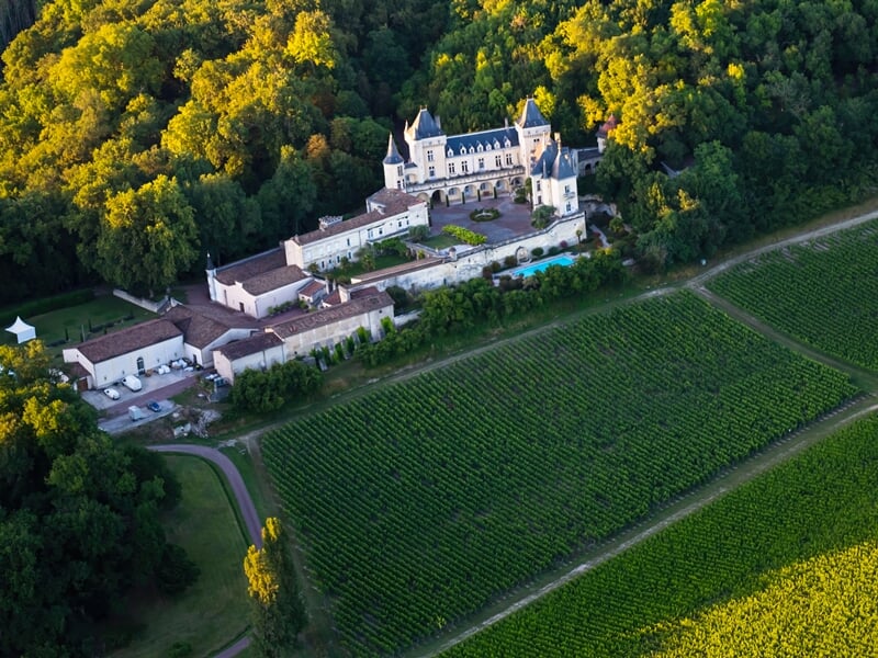 Château bordelais entouré de forêts et de vignobles vu d'en haut au coucher du soleil, avec un éclairage doré qui baigne la scène