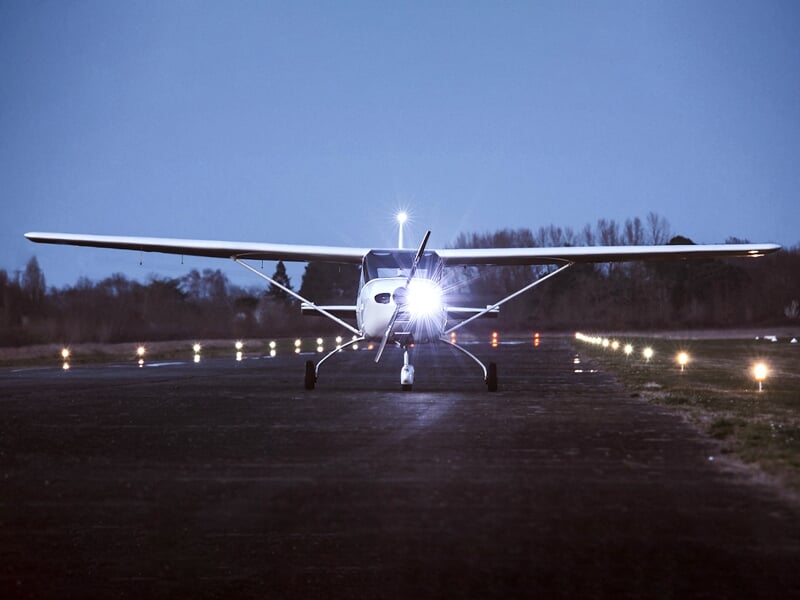 Petit avion avec les lumières d'atterrissage allumées sur une piste au crépuscule, donnant une impression paisible et isolée
