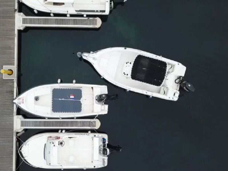 Vue aérienne de trois petits bateaux blancs amarrés parallèlement à un ponton dans un port paisible.