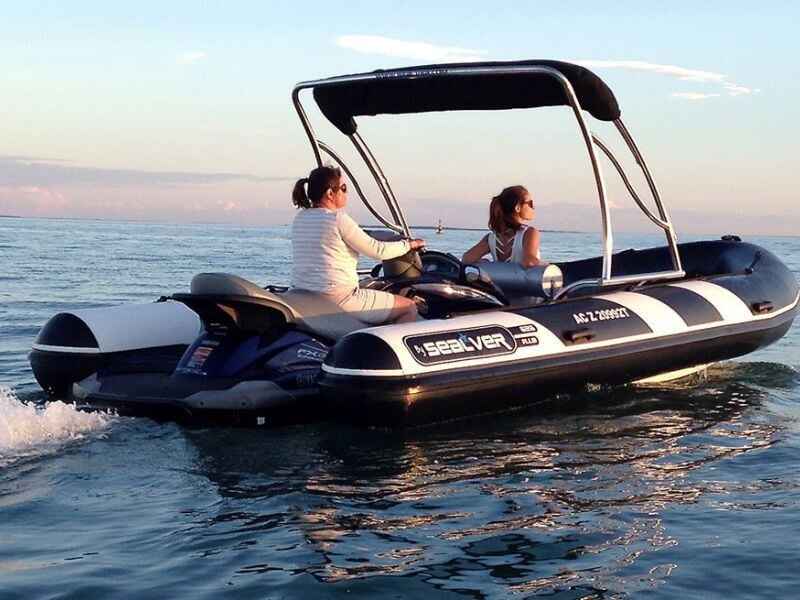 Deux personnes naviguent sur un bateau pneumatique noir et blanc sur une mer calme au coucher du soleil.