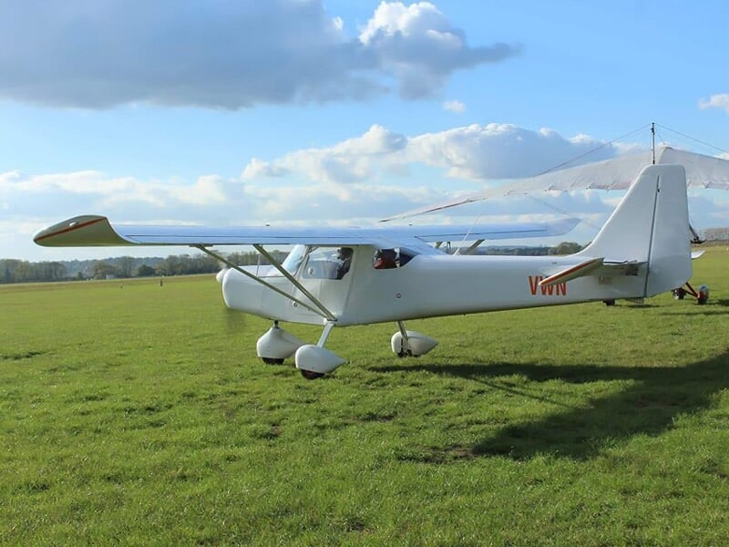 Avion léger blanc immatriculé F-VWTT posé sur une piste d'herbe verte sous un ciel partiellement nuageux.