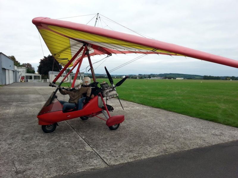 ULM rouge et jaune stationné sur une piste en béton à l'aérodrome de Meaux-Esbly sous un ciel nuageux.