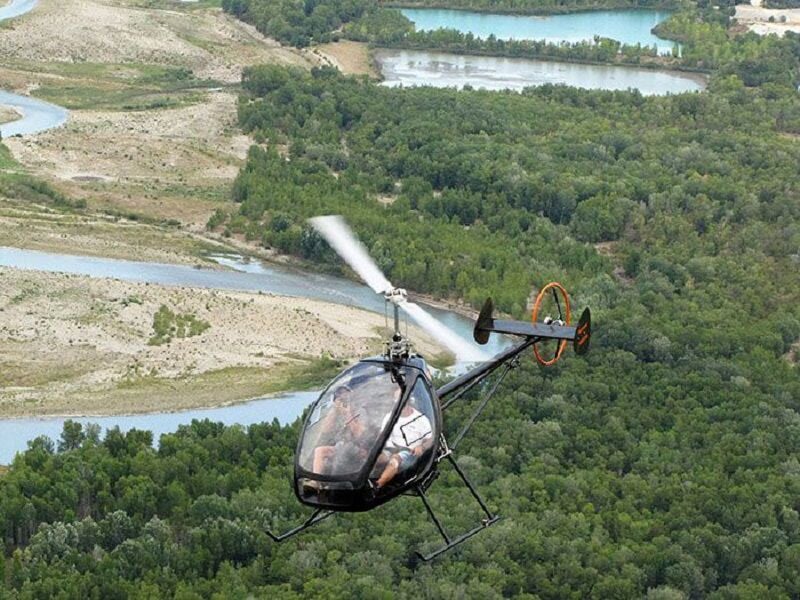 Autogire en vol au-dessus d'une rivière sinueuse et d'une forêt dense vue de haut.