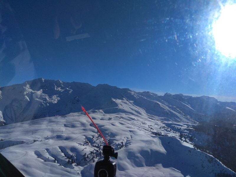 Vue depuis un cockpit sur des montagnes enneigées sous un ciel bleu lumineux.