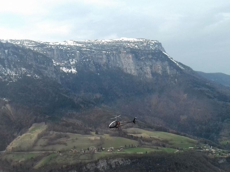 Autogire volant au-dessus d'une vallée avec des falaises et des zones boisées.