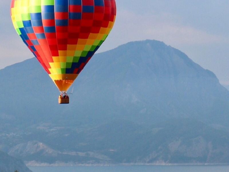 Montgolfière colorée avec motifs en damier survolant une montagne imposante sous un ciel nuageux.
