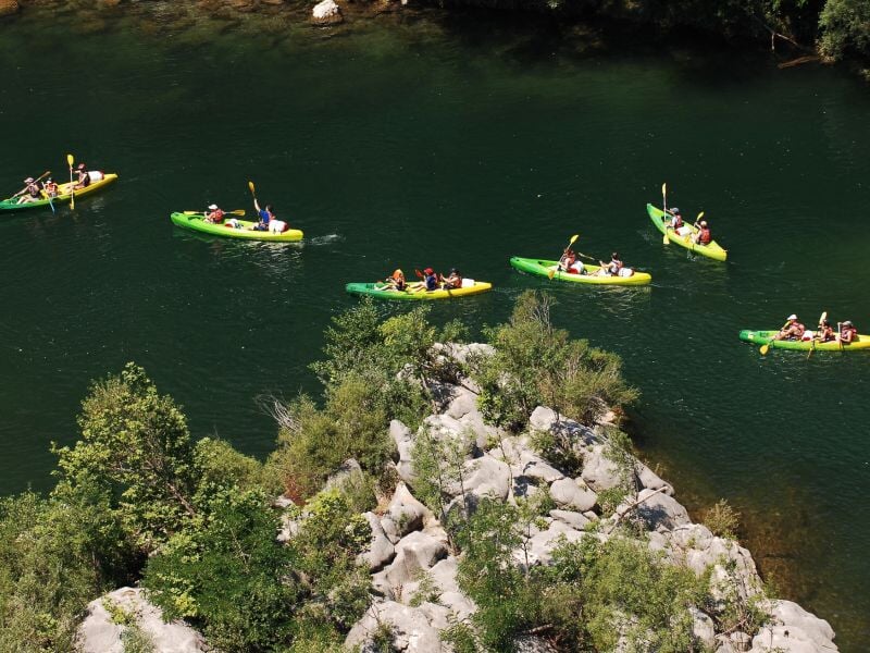 Des personnes pagayant en canoës colorés sur une rivière calme entourée de rochers et de végétation dense.