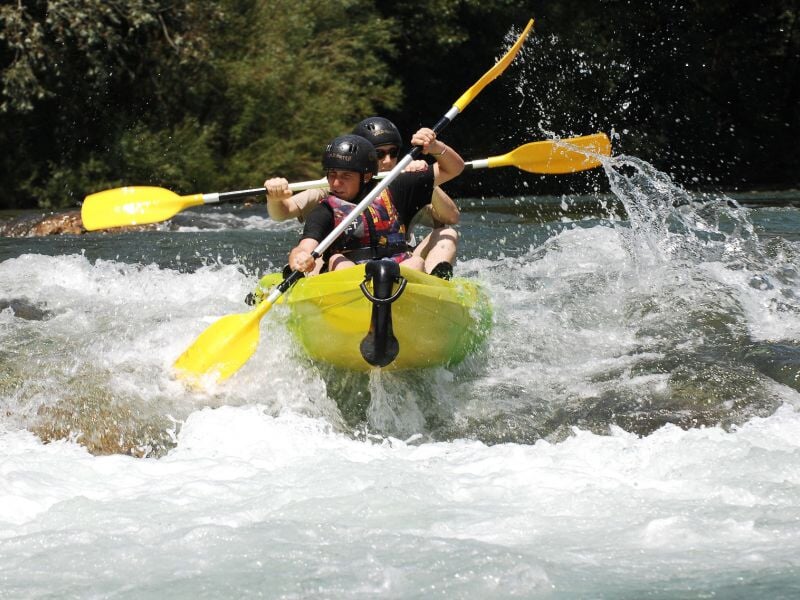 Deux personnes en kayak jaune affrontant des rapides avec éclaboussures d'eau vive sous un ciel clair.